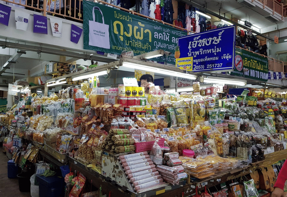 Local Thai market stall in Chiang Mai selling traditional northern snacks, dried fruits, spices, and regional food products with colorful signs and a variety of goods neatly displayed.