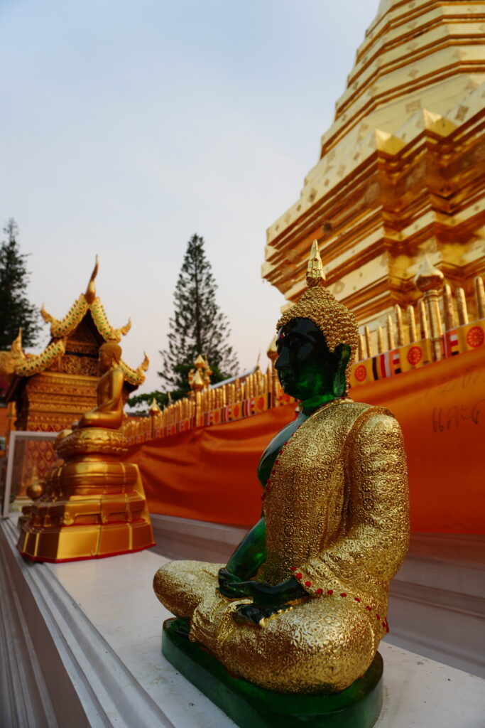 a statue of a replicated emerald buddha with background of the golden pagoda at Wat Phratad Doi Suthep