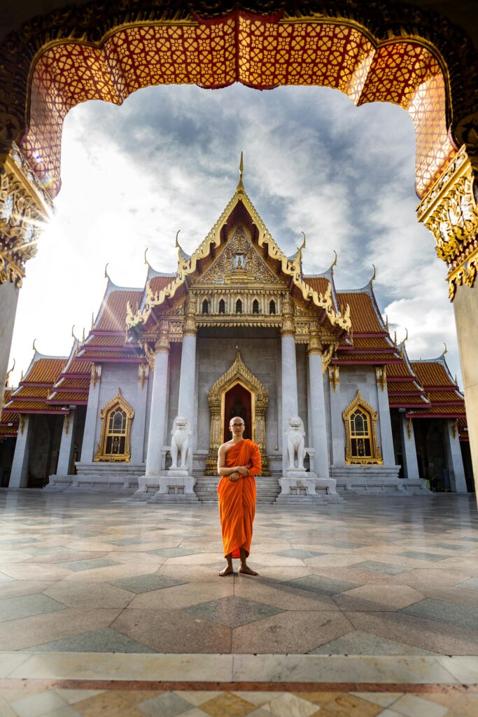 a buddhist monk standing infront of the beautiful decorated temple.